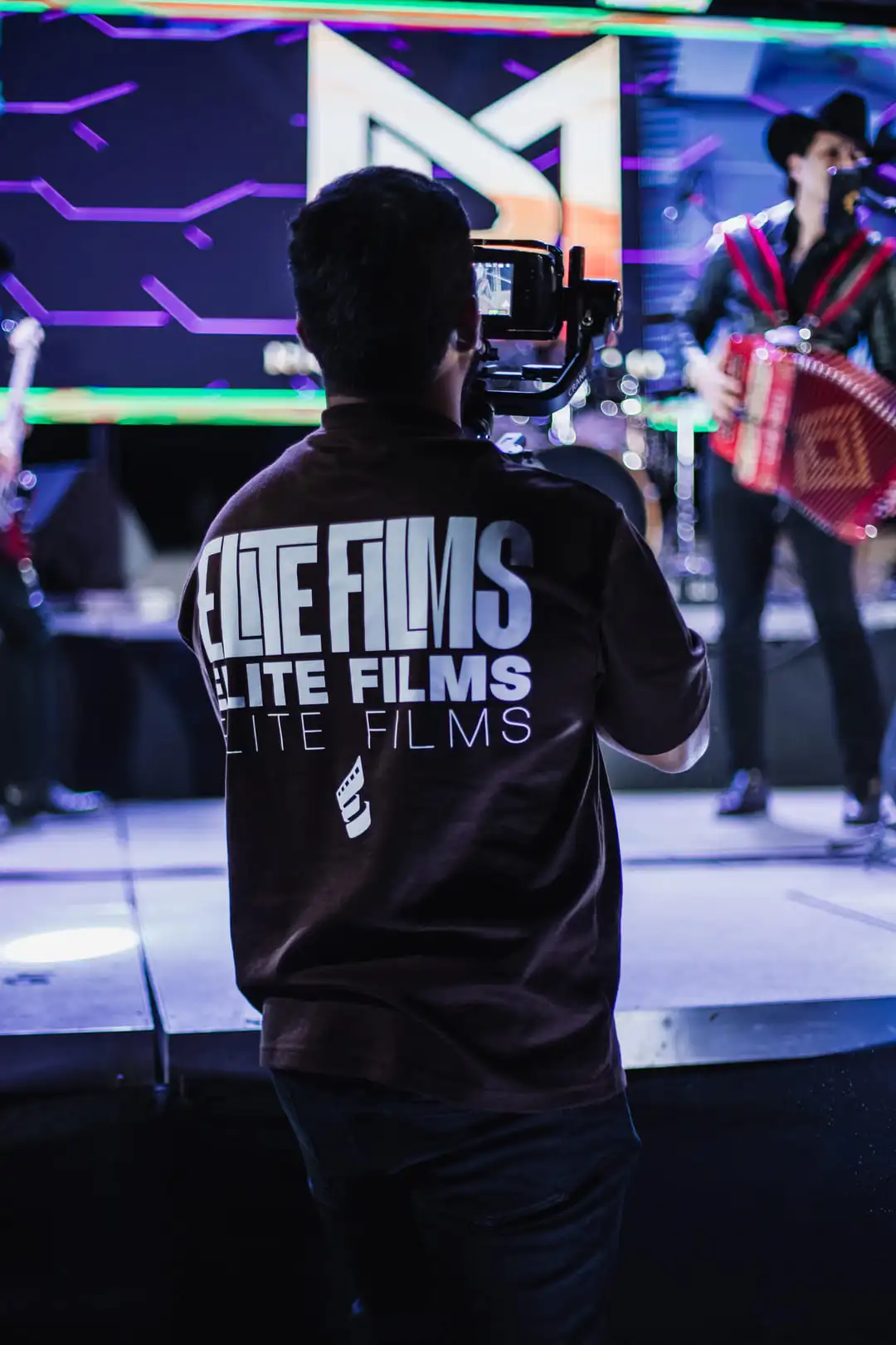 Camarógrafo de Elite Films grabando un evento en vivo con un músico tocando el acordeón en el escenario